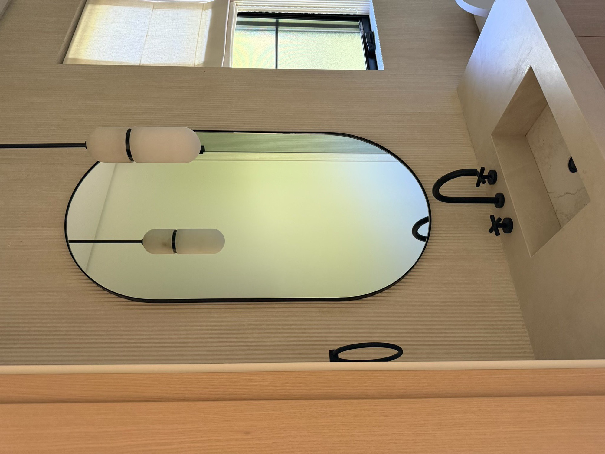 Tall oval black-framed custom mirror above a stone vanity with matte black fixtures